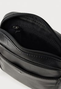 Μαύρη δερμάτινη τσάντα με φερμουάρ, με υφή στην επιφάνεια και εσωτερική θήκη, που παρουσιάζει λείο επένδυση και εμπρόσθια εξωτερική θήκη.