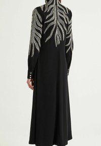 Abito lungo nero con ricami intricati a motivo di foglie bianche lungo le spalle e la schiena, caratterizzato da polsini con bottoni e un colletto alto.