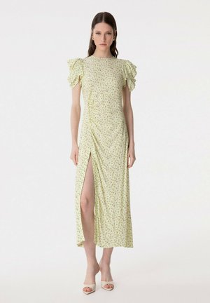 Donna che indossa un vestito midi floreale giallo chiaro con maniche corte a sbuffo e uno spacco alto sulla coscia, abbinato a tacchi aperti beige.