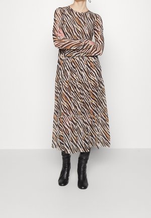 Woman wearing a long-sleeve, tiered animal-print midi dress with black knee-high leather boots, standing with arms crossed.