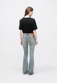 Μαύρο βαμβακερό μπλουζάκι με κοντά μανίκια, συνδυασμένο με ανοιχτό μπλε τζιν παντελόνι καμπάνα, με διακριτική ξεθώριαση και ετικέτα στη ζώνη στην πλάτη.