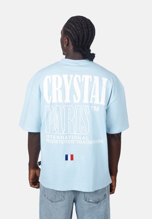 Helles blaues Oversize-T-Shirt aus Baumwolle. Mit großem weißen Text "CRYSTAL PARIS" auf dem Rücken und einem kleinen Detail der französischen Flagge.