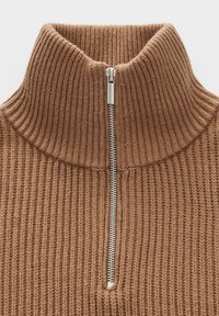 Brauner, gerippter Strickpullover mit hohem Kragen und einem silbernen Halb-Reißverschluss in der Mitte vorne.