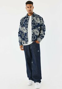 Giacca nel modello paisley blu marina, in vestibilità loose, abbinata a jeans scuri e sneakers bianche. Tessuto morbido; design casual.