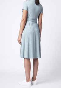 Ljusblå klänning med korta ärmar, en åtsittande midja och en utsvängd kjol. Har ett prickigt mönster och bärs med vita sneakers.