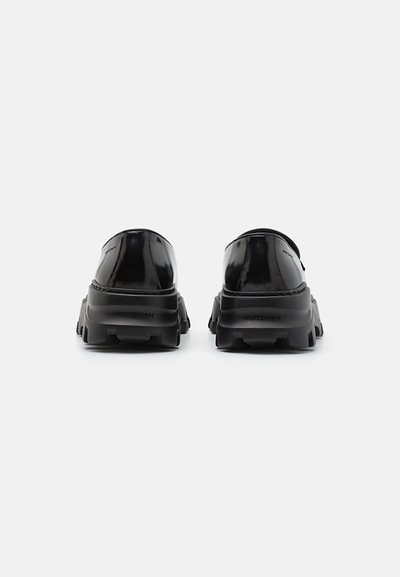 Mocassins en cuir verni noir avec des semelles épaisses et crantées, vus de l'arrière, sur fond blanc uni.