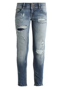 Jean en denim bleu délavé à coupe slim, avec plusieurs patches déchirés et des accents effilochés, denim plus foncé sur le bas des jambes.