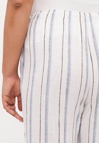 Calças de linho brancas com riscas verticais azuis e castanhas, apresentando uma cintura elástica e um tecido texturizado.