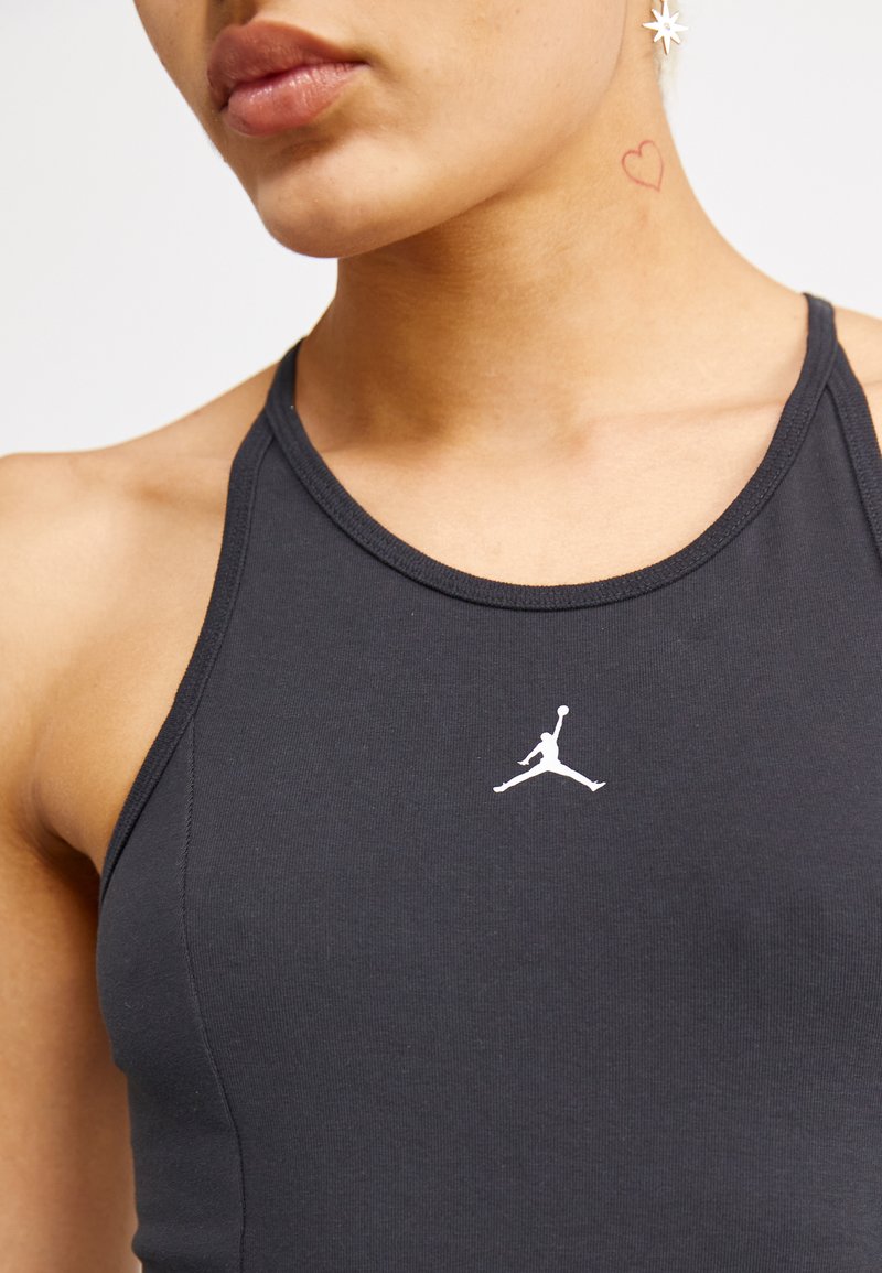 Czarny sportowy top bez rękawów z wysokim dekoltem i cienkimi ramiączkami, z białym logo Jumpman na piersi. Materiał wydaje się gładki i elastyczny.