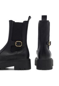 Czarne skórzane botki za kostkę z elastycznymi panelami bocznymi, złotym detalem z klamrą oraz masywną gumową podeszwą. Charakteryzują się gładką fakturą i zaokrąglonym noskiem.