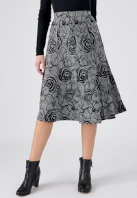 Een uitlopende, knielange rok met een zwart en grijs bloemmotief, gemaakt van gestructureerde stof. Gecombineerd met zwarte enkelboots.