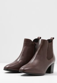 Bottines en cuir marron avec un bout pointu, des panneaux latéraux en élastique et un talon carré. Texture lisse avec un subtil éclat.
