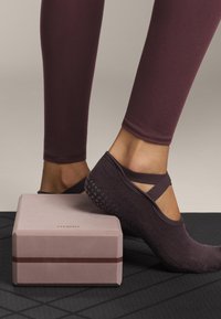 Fleksible bordeaux yoga strømper med stropdetalje, parret med en lyserød yoga blok, der har en kontrasterende mørk stripe og en glat tekstur.