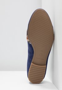 Chaussure en daim bleu marine avec une semelle en caoutchouc brun texturé. Présente un accent coloré à motif sur le côté et un design à bout arrondi.