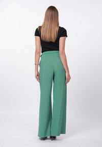 Zelene široke hlače z elastičnim pasom, kombinirane s črno kratkoročnim zgornjim delom, gledano od zadaj. Gladek tekstura tkanine.