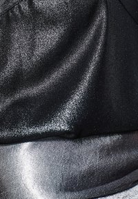Detailní záběr na texturovanou černou a stříbrnou látku s třpytivým, lesklým povrchem a jemnými záhyby.