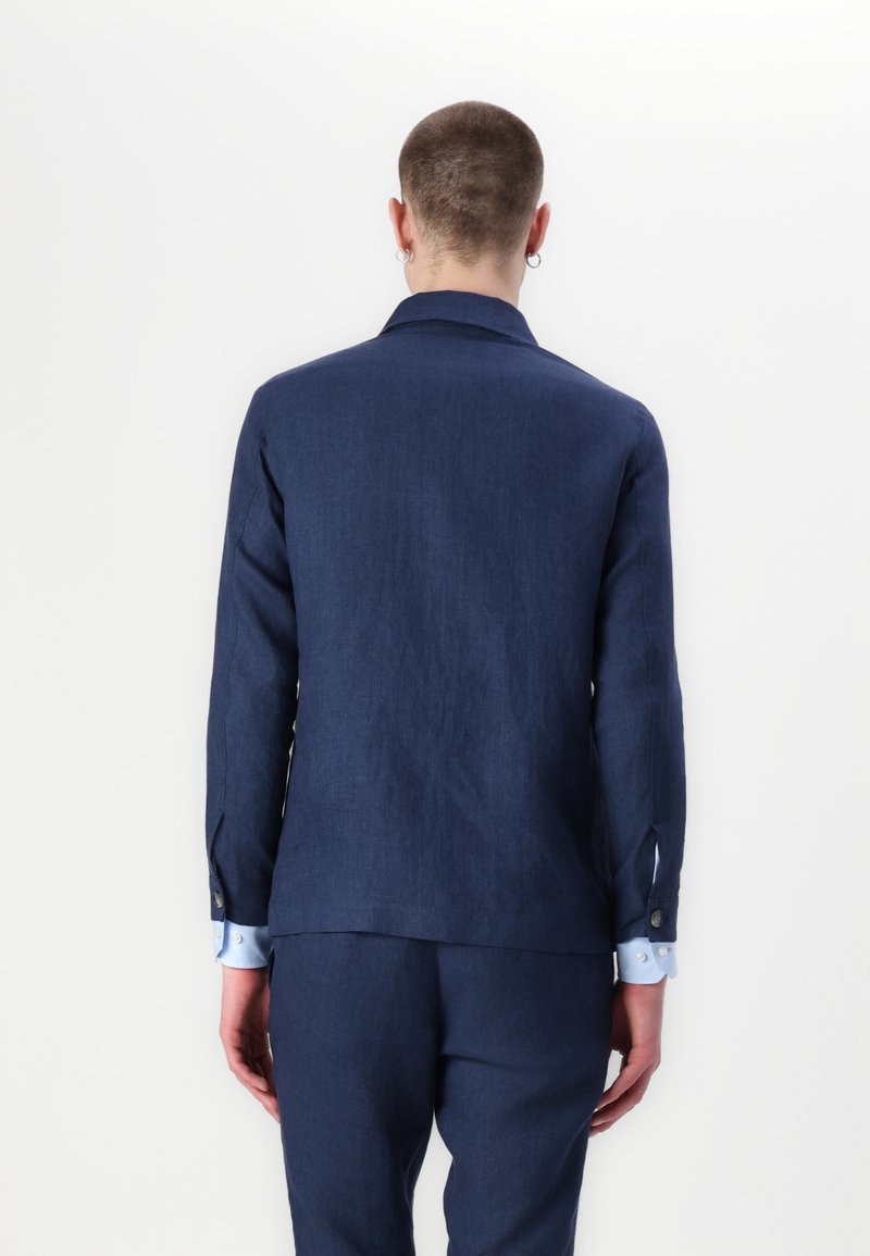 Marineblaues Leinenblazer mit Reverskragen, Ein-Knopf-Verschluss und dezentem Struktur. Ergänzt durch hellblaue Hemdärmel und Knöpfe.