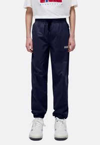Pantalones jogger ligeros en color navy con cintura elástica y puños, que cuentan con bolsillos laterales y un pequeño logo en el muslo izquierdo.