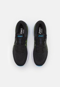 Scarpe da atletica nere con accenti verdi e blu, tomaia in rete, chiusura con lacci e suola bianca con un motivo testurizzato.