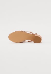 Nude Riemensandalette mit niedrigem Blockabsatz, ausgestattet mit einer strukturierten Sohle und mehreren überlappenden Riemen für einen sicheren Sitz und Komfort.