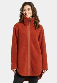 Rustrød fleecejakke med høj krave, fuld frontlynlås og lange ærmer. Har et tekstureret, blødt materiale med en buet kant.