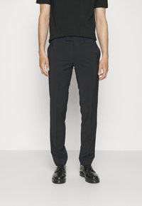 Černé tailored kalhoty s hladkou strukturou a rovnými nohavicemi. V kombinaci s černými šněrovacími botami a přiléhavým černým tričkem.