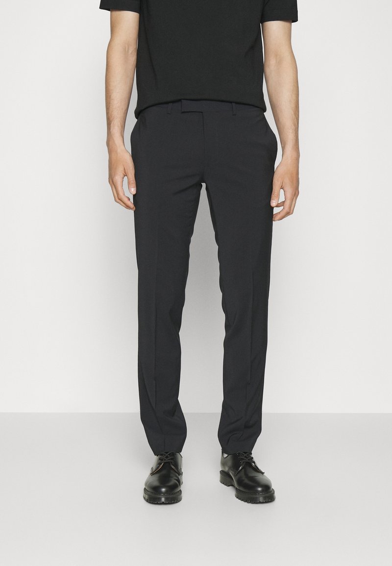 Černé tailored kalhoty s hladkou strukturou a rovnými nohavicemi. V kombinaci s černými šněrovacími botami a přiléhavým černým tričkem.