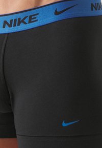 Črne športne bokserice z modrim elastičnim pasom, na katerem je logo "NIKE". Vključujejo majhen modri Nikeov zavihek na tkanini.