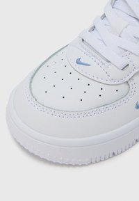 Άσπρο δερμάτινο αθλητικό παπούτσι με διάτρητη μύτη, ανοιχτά γαλάζια στοιχεία, επίπεδα κορδόνια και υφασμένο λάστιχο σόλα με σχέδια σε σχήμα αστεριού.