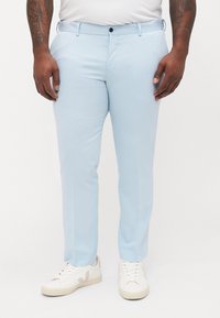 Helle blaue Hose mit glatter Textur, ausgestattet mit flachem Bund, Gürtelschlaufen und einem einzelnen Knopfverschluss, kombiniert mit weißen Sneakers.