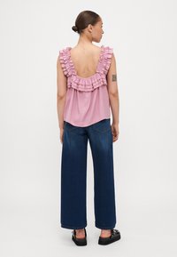 Rosa, ermeløs topp med volanger ved halsen. Kombinert med vide, mørkeblå jeans og svarte platå sko.
