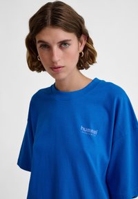 Blå bomullströja med rund halskrage och korta ärmar. Har en subtil logo i ljusare blått på vänster bröst. Mjuk textur.