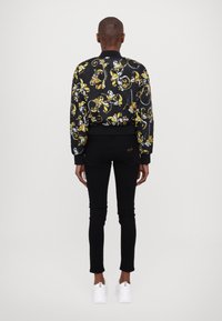 Black floral bomber jacket with yellow and white patterns, ribbed cuffs, paired with black slim-fit jeans and white sneakers.