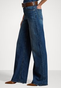 Bredde benjeans i mørkeblå denim med høy midje, utstyrt med et brunt lærbelte, og rene, frynsete detaljer nederst.