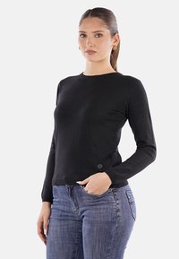 Maglietta nera a maniche lunghe con scollo rotondo, caratterizzata da una superficie testurizzata e un piccolo bottone decorativo sull'orlo, abbinata a jeans blu.