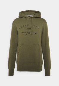 Sweat à capuche vert olive en tissu doux, avec une poche kangourou à l'avant, un cordon de serrage à la capuche et un texte imprimé : "BJÖRN BORG 1956 STOCKHOLM."