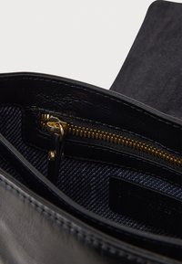 Intérieur d'un sac à main en cuir noir avec une fermeture éclair en or, une doublure en denim et une texture lisse. Mobilier visible et détails d'accent inclus.