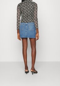 Haut à manches longues noir et blanc à motif, associé à une mini-jupe en denim bleu, avec un ourlet effiloché et des poches arrière. Chaussures noires à enfiler.