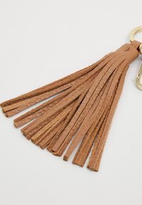 Porte-clés en cuir tan avec plusieurs longues stries étroites, attaché à un anneau en métal doré. La texture est lisse avec une légère brillance.