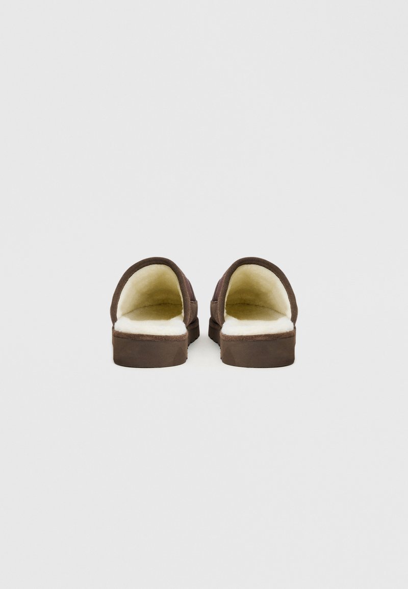 Braune Hausschuhe zum Hineinschlüpfen mit einem weichen, cremefarbenen Futter und einer flachen Sohle. Das Design ist schlicht und ohne zusätzliche Verzierungen.