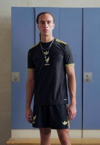 Fekete sportmez arany részletekkel és "MEXIKÓ" felirattal, párosítva hozzáillő fekete sorttal. Textúrával ellátott mintázatokkal és logó részletekkel rendelkezik.