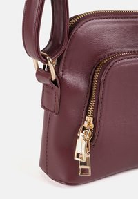 Borsa in finta pelle bordeaux con zipper e componenti dorati, caratterizzata da una forma strutturata e una maniglia corta per il trasporto.