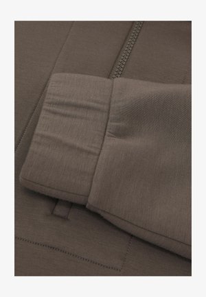 Braunes, zum Schließen mit Reißverschluss versehenes Hemd mit glatter Textur, dezentem Glanz und Manschette mit genähten Details. Der Reißverschluss verläuft vertikal in der Mitte.