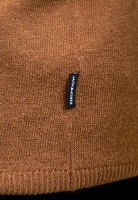 Cappello berretto lavorato a maglia marrone con orlo a costine. Presenta un'etichetta nera con la scritta "JACK & JONES" in bianco sul lato. Texture morbida.