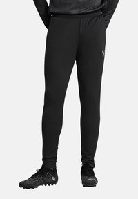 Zwarte sportbroek met een taps toelopende pasvorm, elastische tailleband en subtiele branding. Gecombineerd met zwarte voetbalschoenen met een gestructureerd ontwerp.