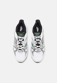 Białe buty sportowe z zielonymi i czarnymi akcentami, z siateczkową cholewką, wyściełanym kołnierzem oraz białą podeszwą o teksturowanym wzorze.