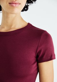 Bordo kratki sleev t-shirt s krojem, izdelan iz mehkega in gladkega blaga; vsebuje šive ob robovih.