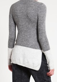 Grauer gestrickter Pullover mit langen Ärmeln, der einen hellgrauen Saum hat. Die Textur wirkt weich und das Design ist lässig mit einem runden Ausschnitt.