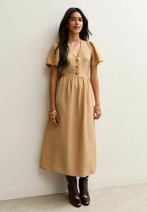 Beige midi-jurk met korte pofmouwen, knopen aan de voorkant en gathered taille. Gediende met bruin, kniehoge laarzen. Soepele textuur, subtiel patroon.