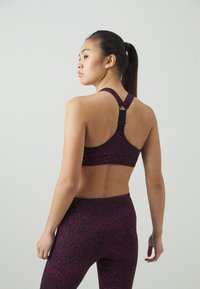 Αθλητικό σουτιέν σε σκούρο μωβ με υφασμάτινο σχέδιο, διαθέτοντας σχέδιο με διασταυρούμενες πλάτες και ρυθμιζόμενο μηχανισμό στους ιμάντες.